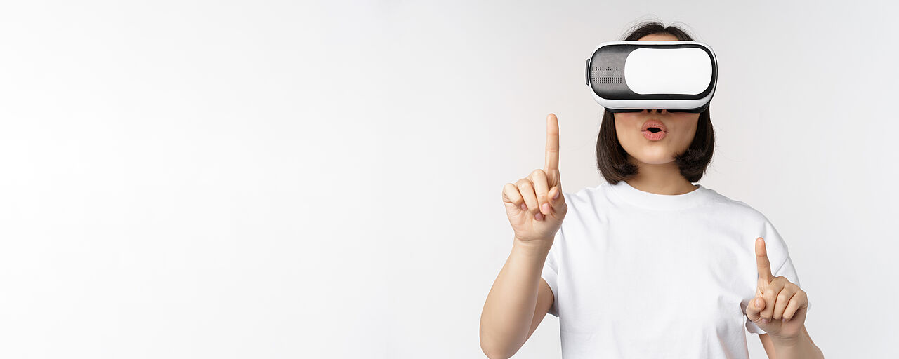 Potrait of asian woman in virtual reality glasses, pointing, choosing smth in VR headset, standing over white background